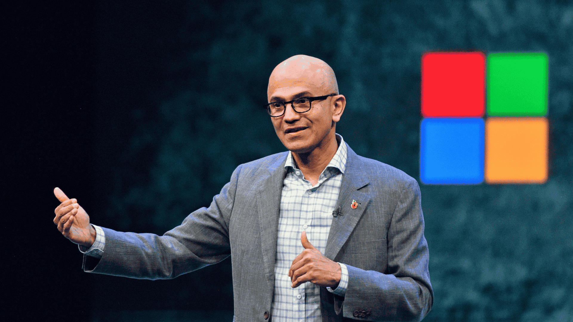 Satya Nadella’s Journey from Microsoft executive to CEO, shown speaking in front of the Microsoft logo.